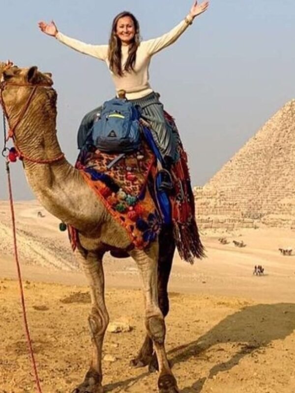 Tourists ride a camel next to the pyramids and sphinx